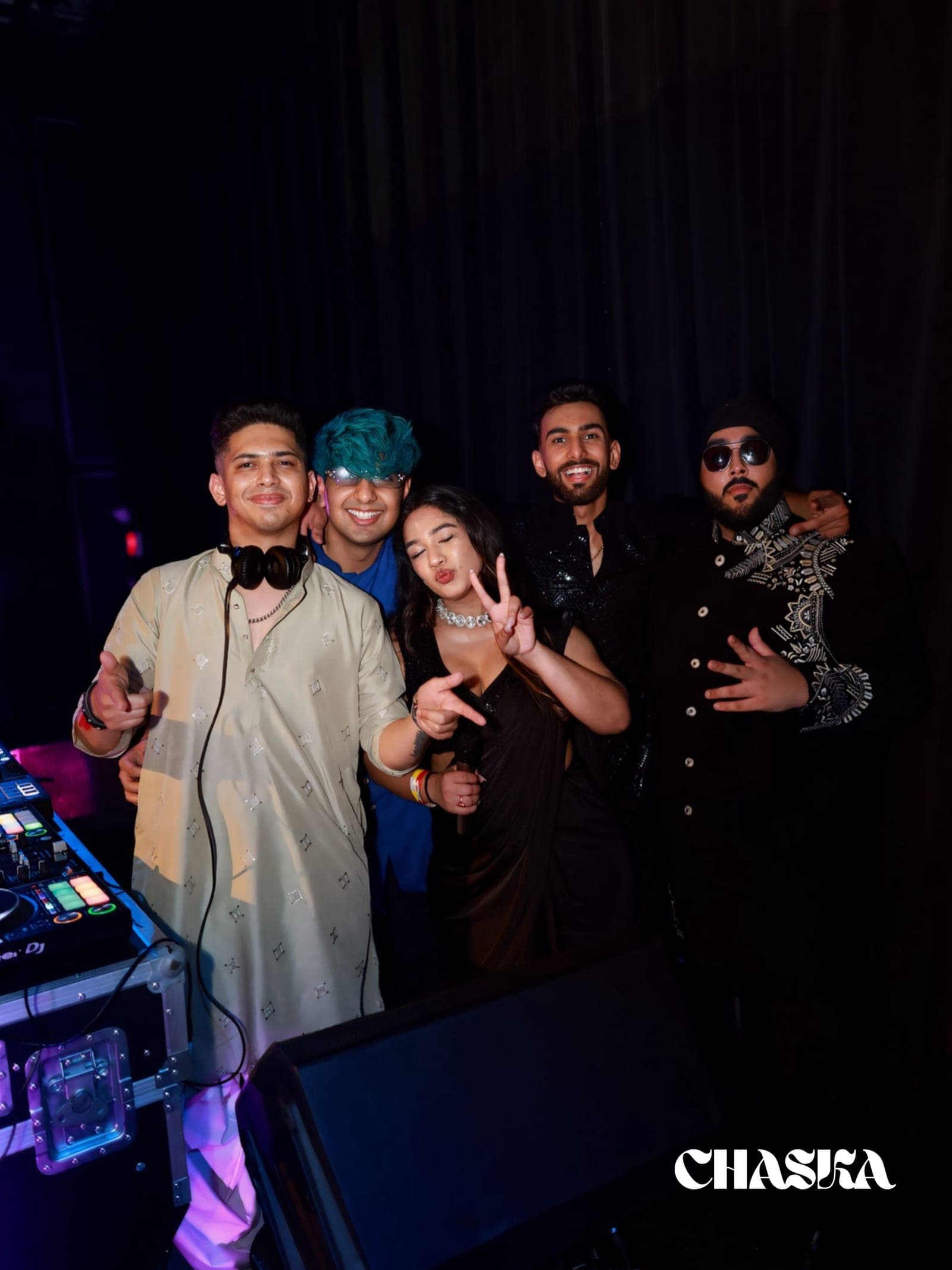 Five friends in South-Asian formalwear beside the DJ decks at a Chaska night